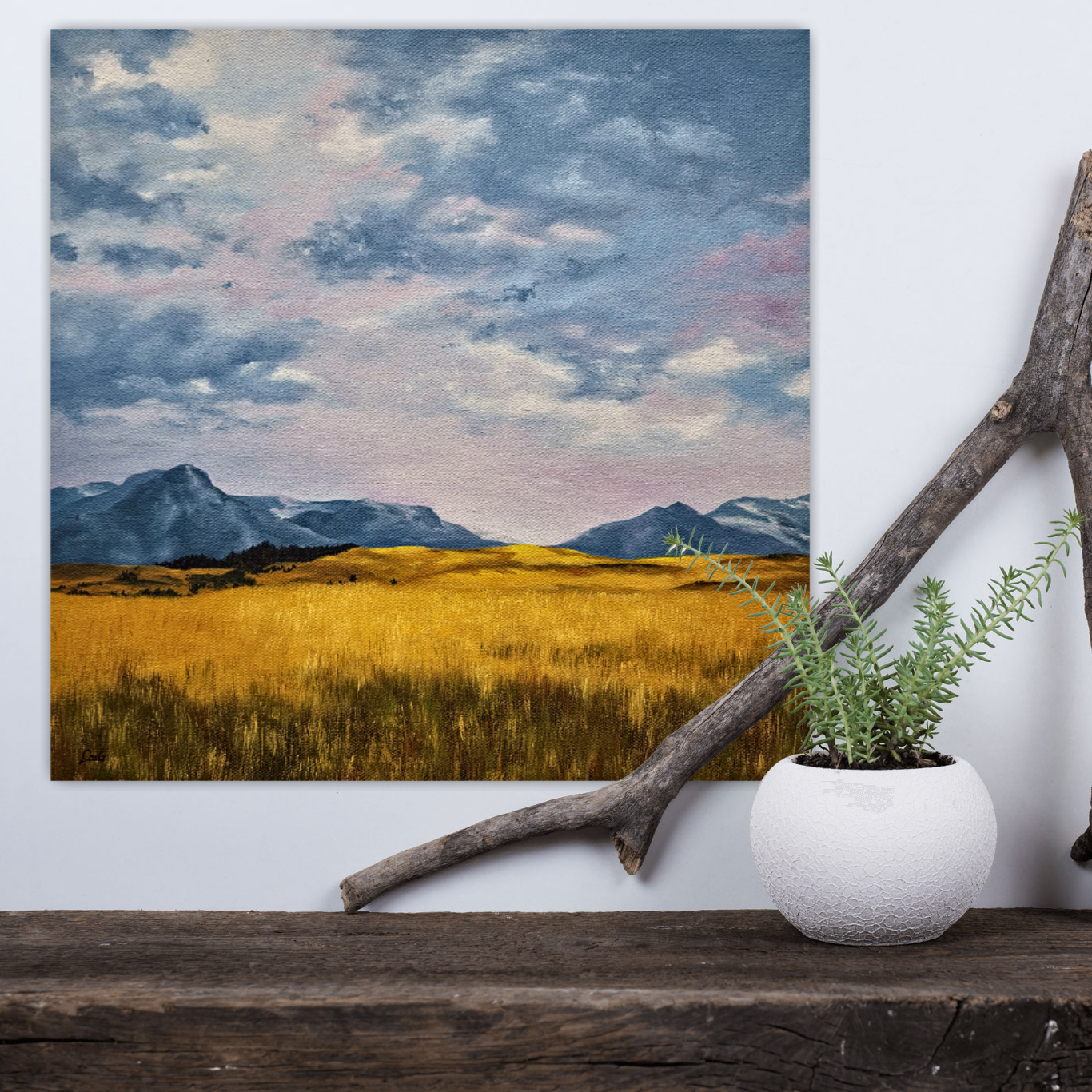 Christina Gouldsborough original oil painting of a wheat field with mountains in the background and lilac hued sky, on a white wall behind a shelf with a plant and driftwood