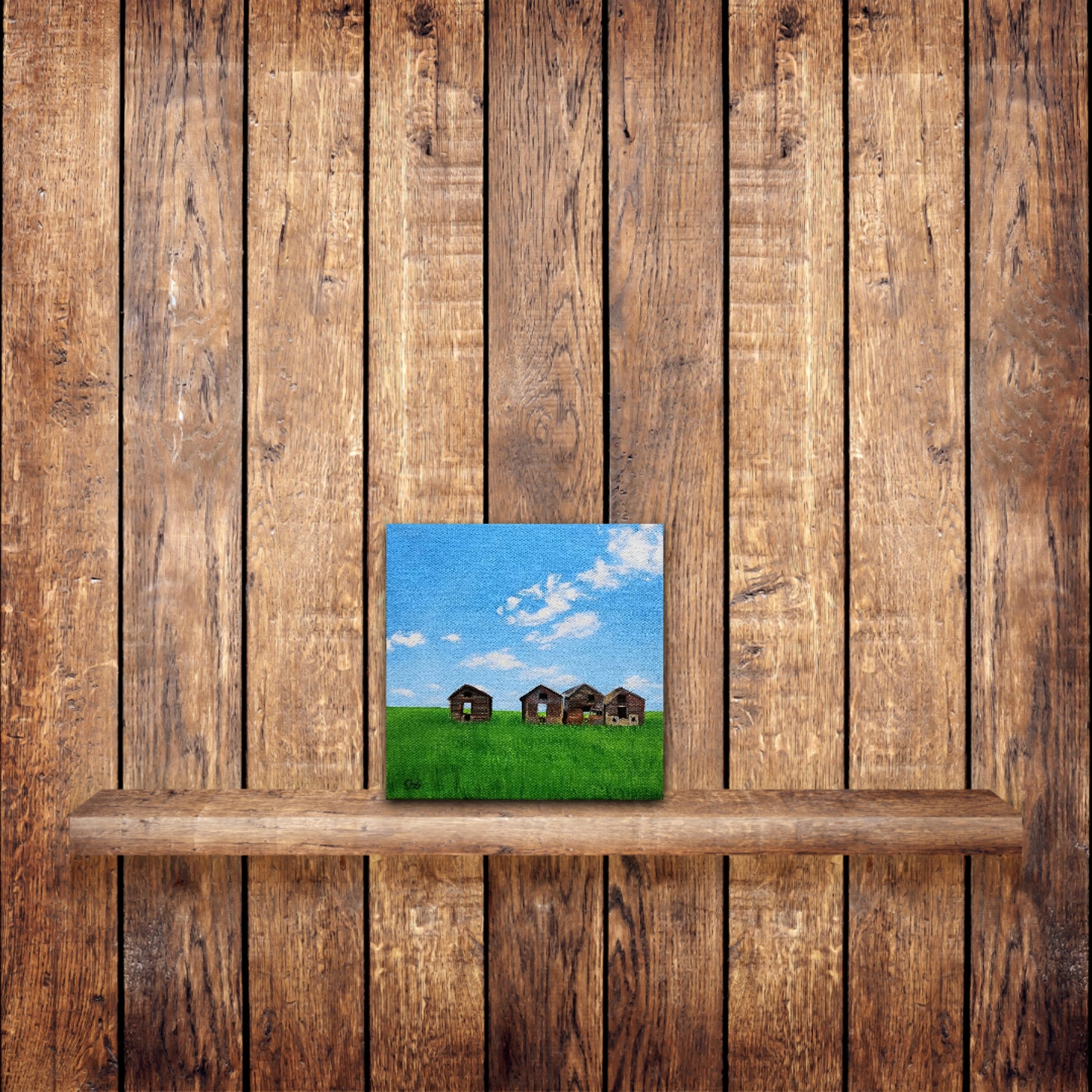 Small, original oil painting of 4 prairie sheds in a green field in summer, in front of wood pine wall and shelf