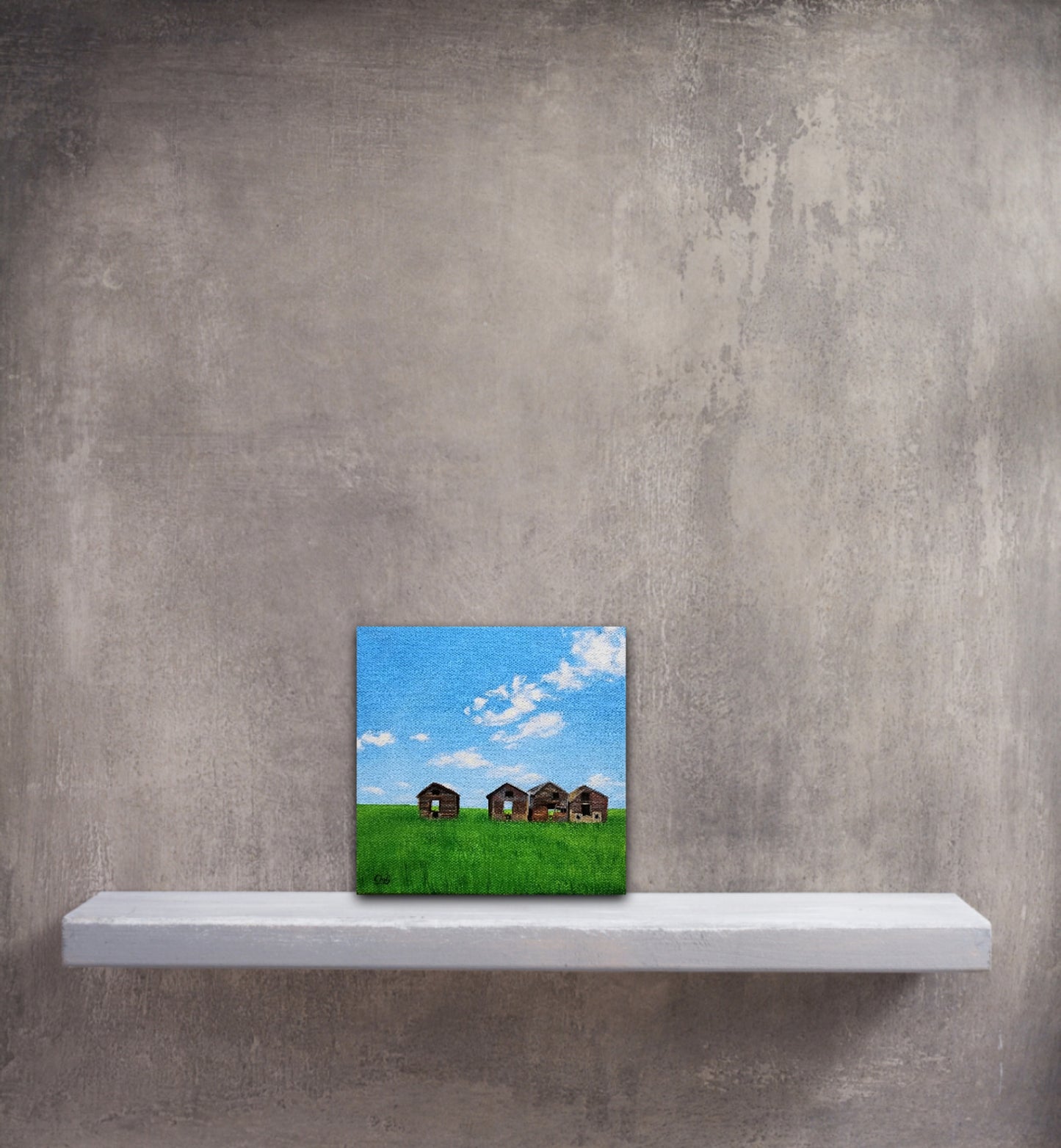 Small, original oil painting of 4 prairie sheds in a green field in summer, in front of grey wall and shelf