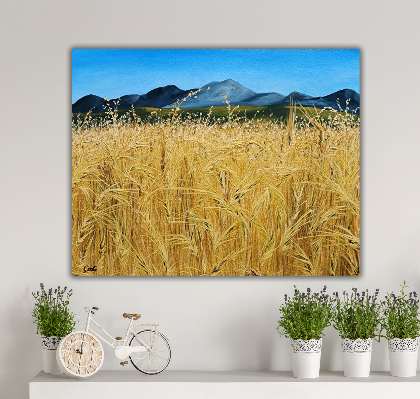 Christina Gouldsborough original oil painting "Picnic In the Wheat" of a up close wheat field with distant mountains in the distance, on a white wall with plants and decorations beneath