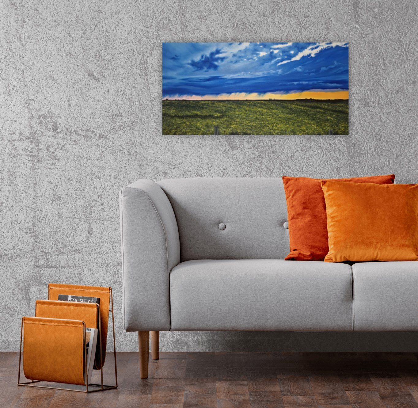 Happy Hour and original oil painting by Christina Gouldsborough of a vibrant sunset after a summer storm over the canola fields , on a grey wall behind a grey couch with orange decor accessories